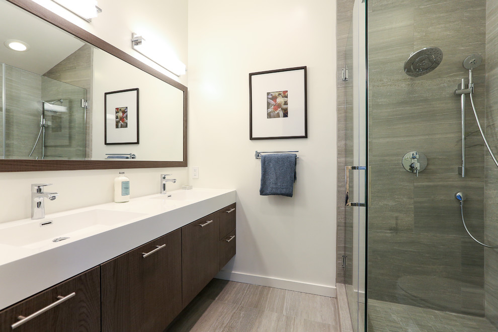 Modelo de cuarto de baño principal actual de tamaño medio con lavabo tipo consola, puertas de armario de madera en tonos medios, ducha esquinera, baldosas y/o azulejos grises y paredes blancas
