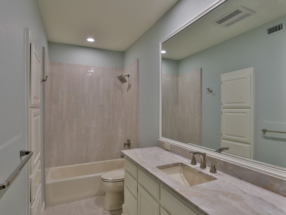Cette image montre une salle de bain avec un placard avec porte à panneau surélevé, un carrelage bleu, un plan de toilette en granite, un plan de toilette bleu, une baignoire posée, une douche double, WC à poser, des carreaux de porcelaine, un mur bleu, un sol en carrelage de porcelaine, un lavabo encastré, un sol beige et aucune cabine.