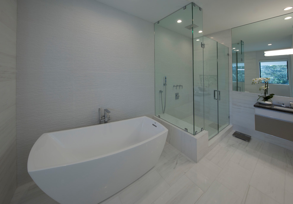 Réalisation d'une salle de bain principale design de taille moyenne avec un placard à porte plane, des portes de placard marrons, une baignoire indépendante, une douche d'angle, un carrelage gris, un mur gris, un lavabo suspendu et un sol blanc.