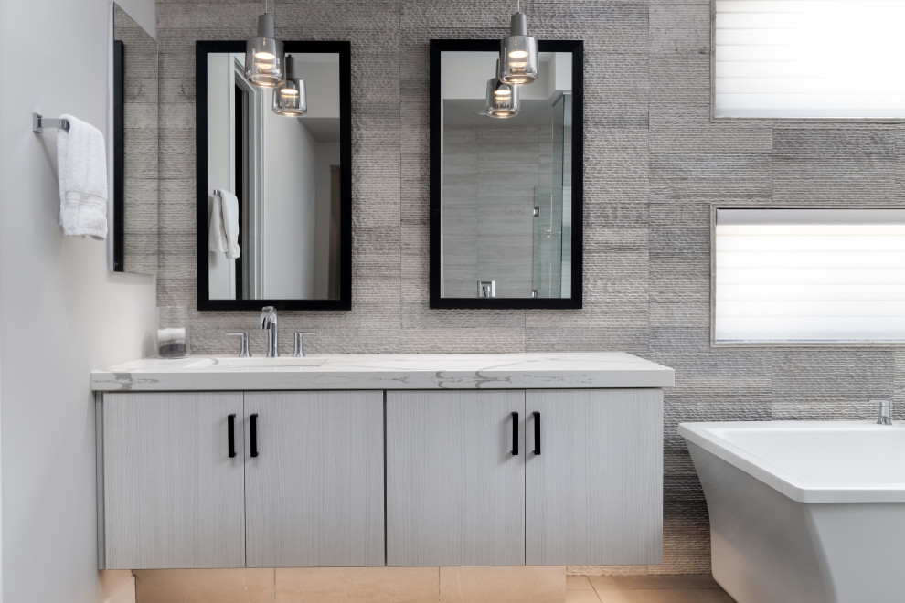 Diseño de cuarto de baño contemporáneo con armarios con paneles lisos, puertas de armario grises, bañera exenta, baldosas y/o azulejos grises, lavabo bajoencimera, suelo gris y encimeras blancas