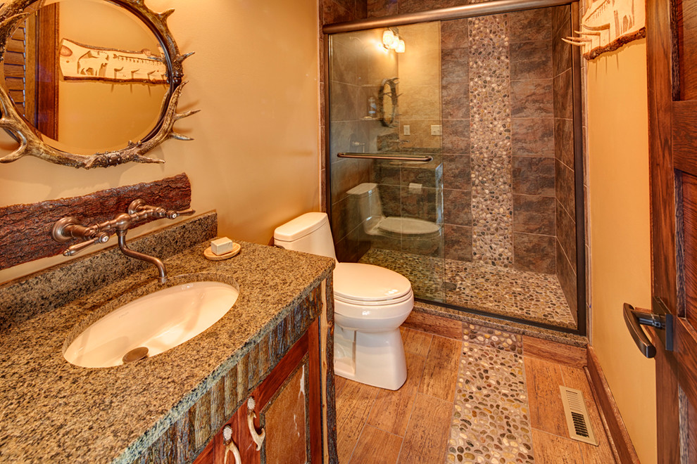 На фото: ванная комната среднего размера в стиле рустика с врезной раковиной, темными деревянными фасадами, столешницей из гранита, коричневой плиткой, галечной плиткой, бежевыми стенами и полом из керамогранита с
