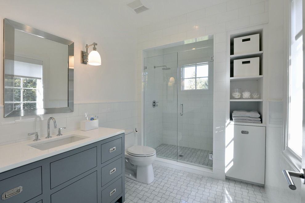 Klassisches Badezimmer mit Unterbauwaschbecken, flächenbündigen Schrankfronten, blauen Schränken, Duschnische, Toilette mit Aufsatzspülkasten, weißen Fliesen und weißer Wandfarbe in New York