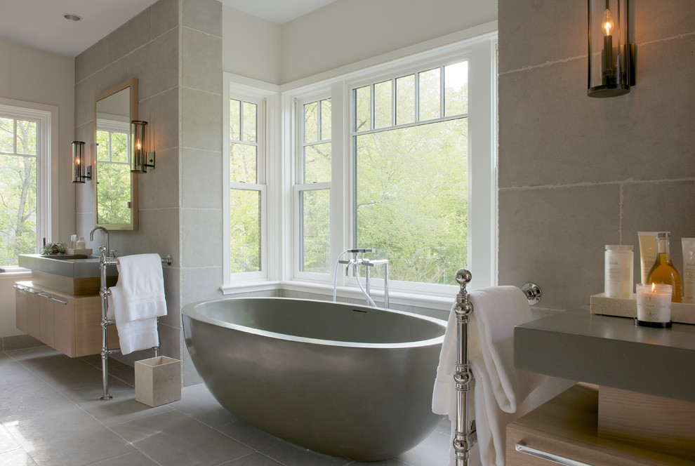 Пример оригинального дизайна: большая главная ванная комната в викторианском стиле с плоскими фасадами, светлыми деревянными фасадами, отдельно стоящей ванной, серой плиткой, цементной плиткой, белыми стенами, врезной раковиной и серой столешницей
