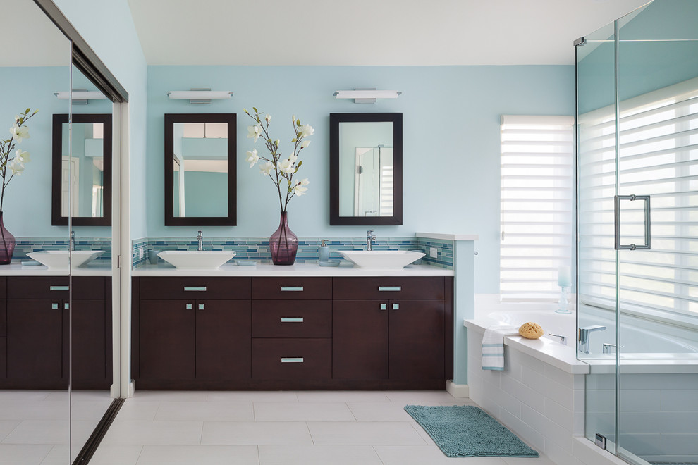 Cette image montre une salle de bain principale design en bois foncé de taille moyenne avec un placard à porte plane, un mur bleu, une vasque, une cabine de douche à porte battante, un sol en carrelage de porcelaine, une baignoire d'angle, une douche d'angle, un carrelage bleu, un plan de toilette en quartz modifié, un carrelage en pâte de verre, un sol blanc et une fenêtre.