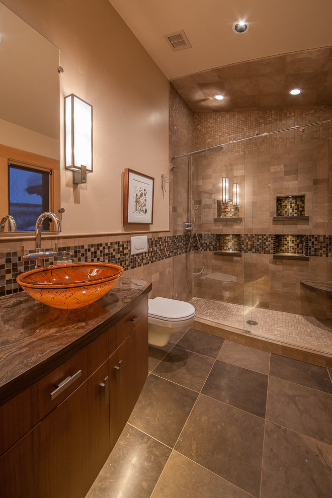 Modern inredning av ett mellanstort brun brunt badrum med dusch, med ett fristående handfat, släta luckor, skåp i mellenmörkt trä, en dusch i en alkov, en vägghängd toalettstol, brun kakel, mosaik, beige väggar, klinkergolv i porslin, marmorbänkskiva, grått golv och dusch med gångjärnsdörr
