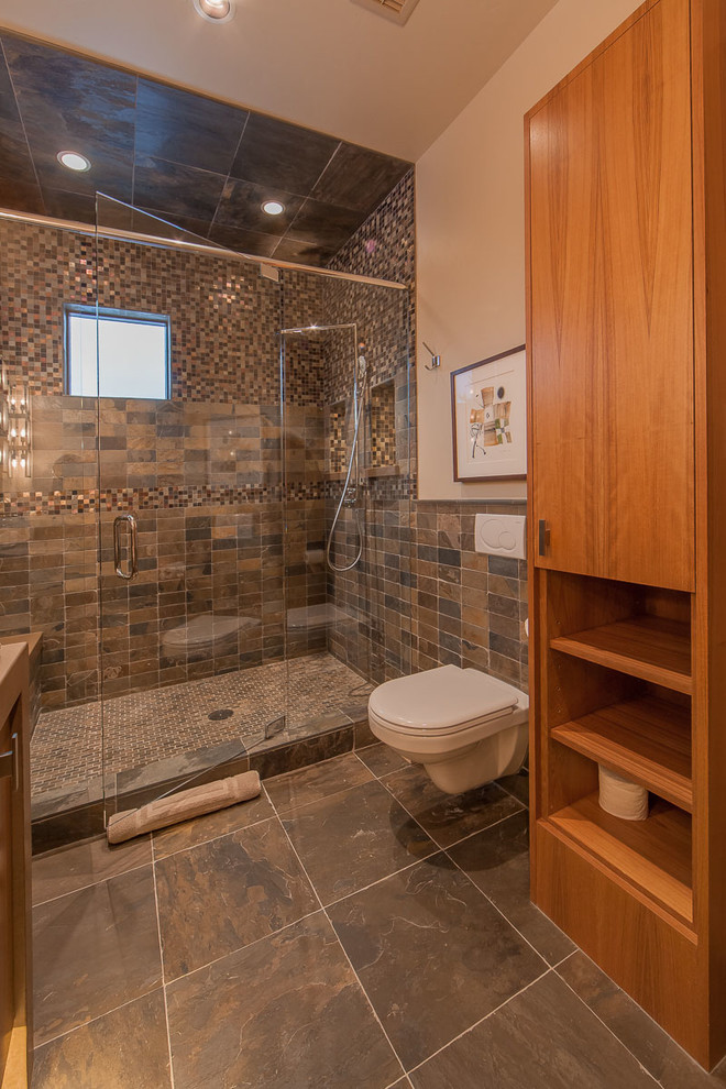 Inspiration for a medium sized contemporary shower room bathroom in Denver with flat-panel cabinets, medium wood cabinets, an alcove shower, a wall mounted toilet, brown tiles, mosaic tiles, beige walls, porcelain flooring, a vessel sink, marble worktops, grey floors and a hinged door.