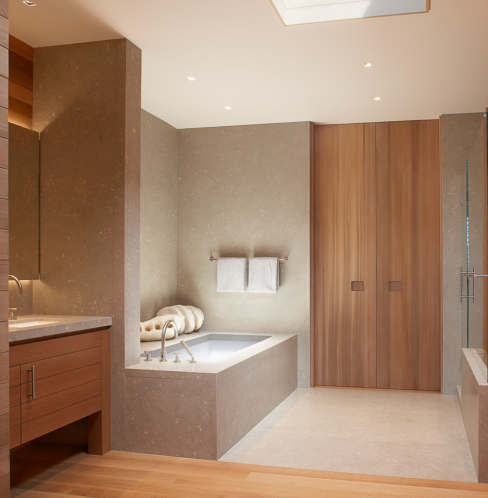 Large contemporary ensuite bathroom in San Francisco with a submerged sink, flat-panel cabinets, medium wood cabinets, granite worktops, a corner bath, a corner shower, beige tiles, stone tiles, beige walls and light hardwood flooring.