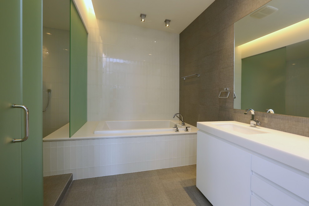 Inspiration pour une salle de bain design avec un lavabo encastré, un placard à porte plane, des portes de placard blanches, un plan de toilette en surface solide, une baignoire posée, WC à poser et un carrelage gris.