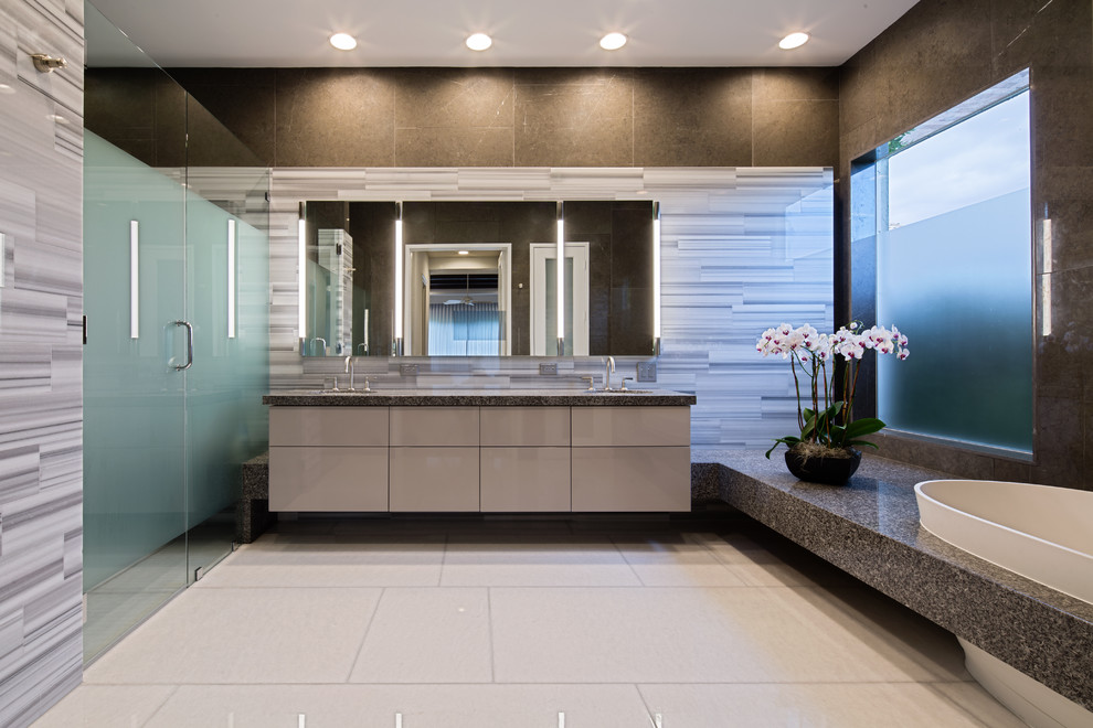 Photo of an expansive classic ensuite bathroom in Miami with a submerged sink, flat-panel cabinets, grey cabinets, granite worktops, a freestanding bath, a corner shower, a one-piece toilet, grey tiles, stone slabs, grey walls and marble flooring.
