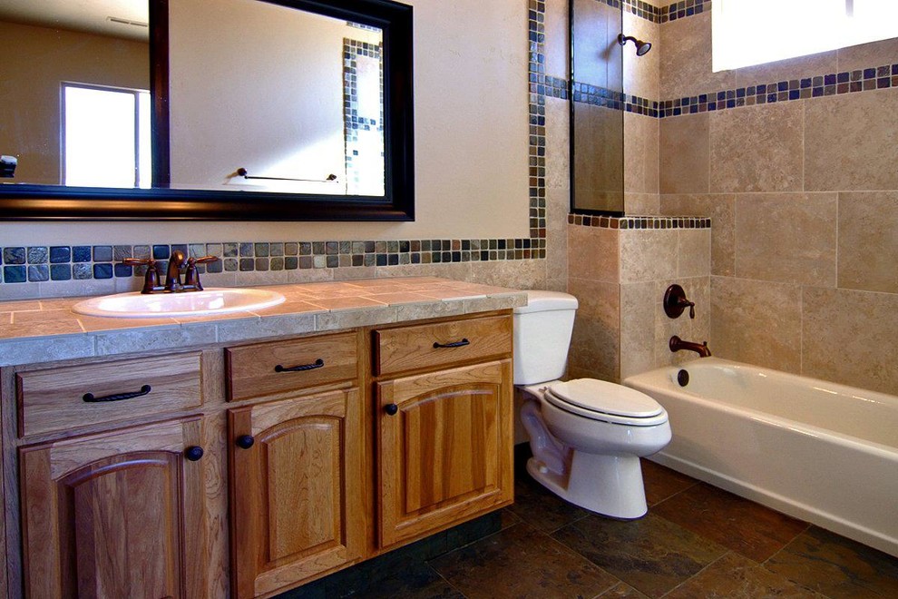 Inspiration for a mid-sized mediterranean 3/4 beige tile and porcelain tile slate floor tub/shower combo remodel in Salt Lake City with a drop-in sink, raised-panel cabinets, medium tone wood cabinets, tile countertops, a two-piece toilet and beige walls