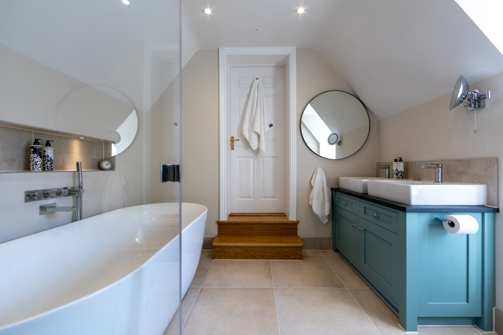 Photo of a large traditional ensuite bathroom in Surrey with shaker cabinets, blue cabinets, a freestanding bath, a corner shower, grey tiles, porcelain tiles, beige walls, porcelain flooring, a vessel sink, beige floors, an open shower, black worktops, double sinks, a built in vanity unit and a wall niche.