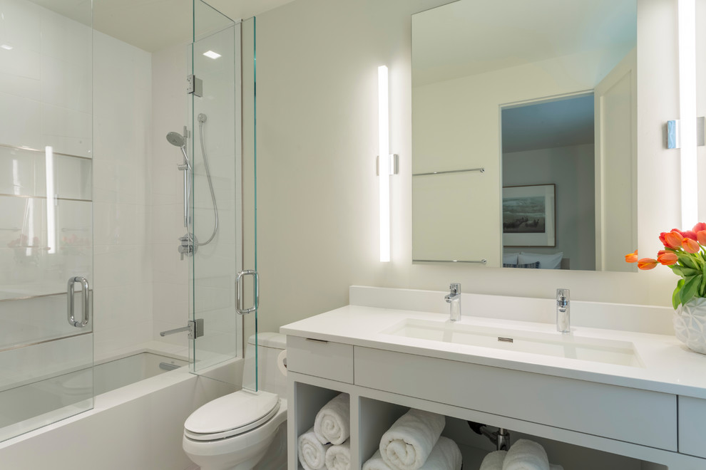 Пример оригинального дизайна: ванная комната среднего размера в стиле модернизм с открытыми фасадами, белыми фасадами, ванной в нише, душем над ванной, унитазом-моноблоком, белой плиткой, керамогранитной плиткой, бежевыми стенами, полом из керамогранита, душевой кабиной, врезной раковиной, столешницей из искусственного кварца и душем с распашными дверями