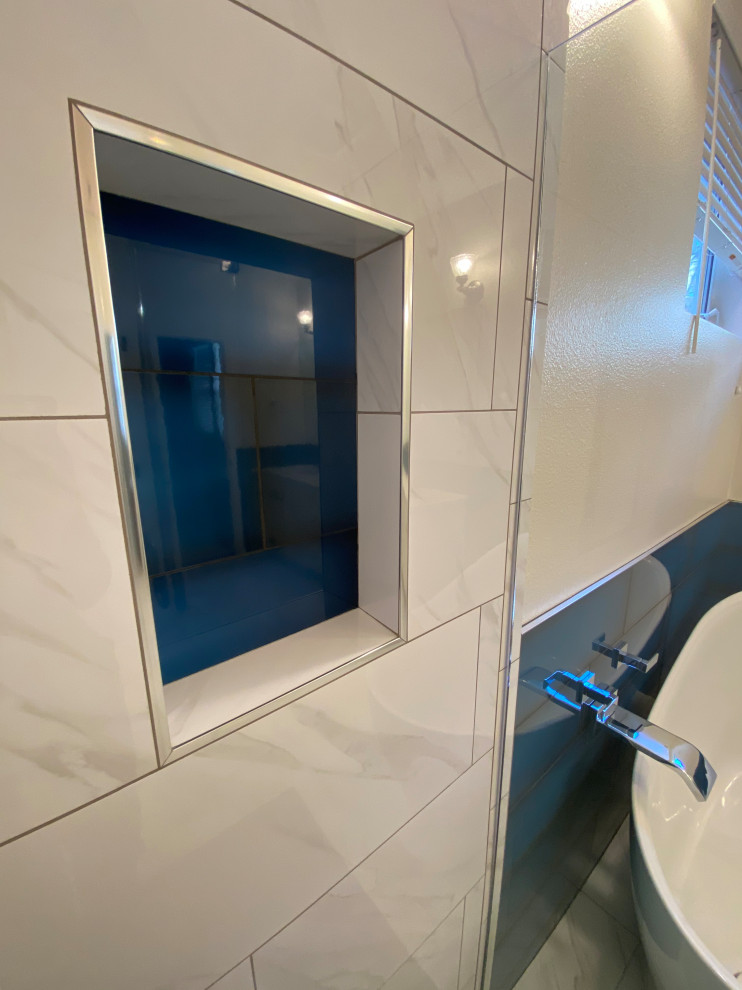 Photo of a contemporary ensuite bathroom in Seattle with recessed-panel cabinets, white cabinets, a freestanding bath, a corner shower, a one-piece toilet, blue tiles, ceramic tiles, white walls, porcelain flooring, a submerged sink, engineered stone worktops, white floors, a hinged door, white worktops, a wall niche, double sinks, a built in vanity unit and wainscoting.