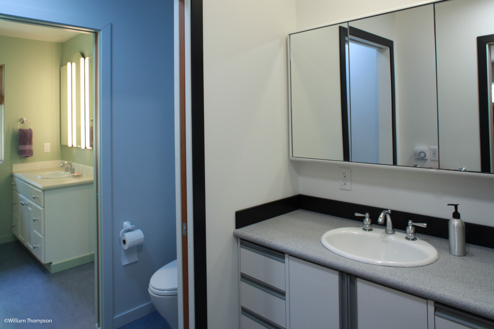 Mid-sized transitional kids' linoleum floor, blue floor and single-sink alcove shower photo in Seattle with a drop-in sink, flat-panel cabinets, white cabinets, solid surface countertops, a two-piece toilet, white walls, gray countertops, a built-in vanity and a hinged shower door