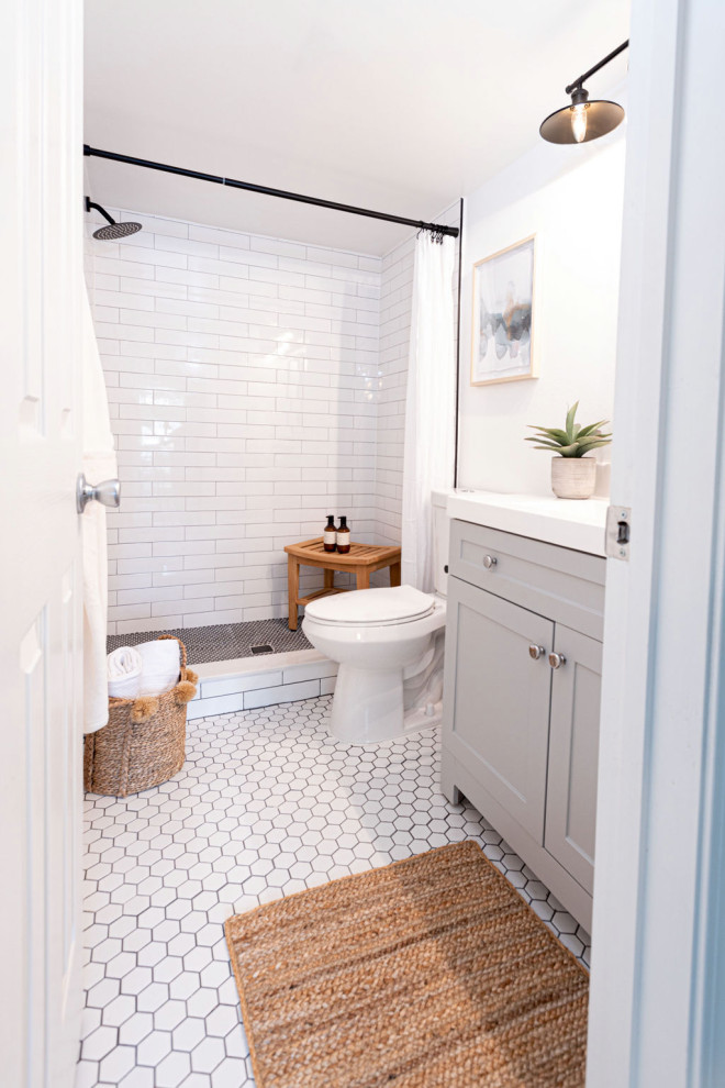 Lantlig inredning av ett litet vit vitt en-suite badrum, med grå skåp, en toalettstol med hel cisternkåpa, vit kakel, porslinskakel, grå väggar, klinkergolv i porslin, bänkskiva i kvartsit, vitt golv och dusch med duschdraperi
