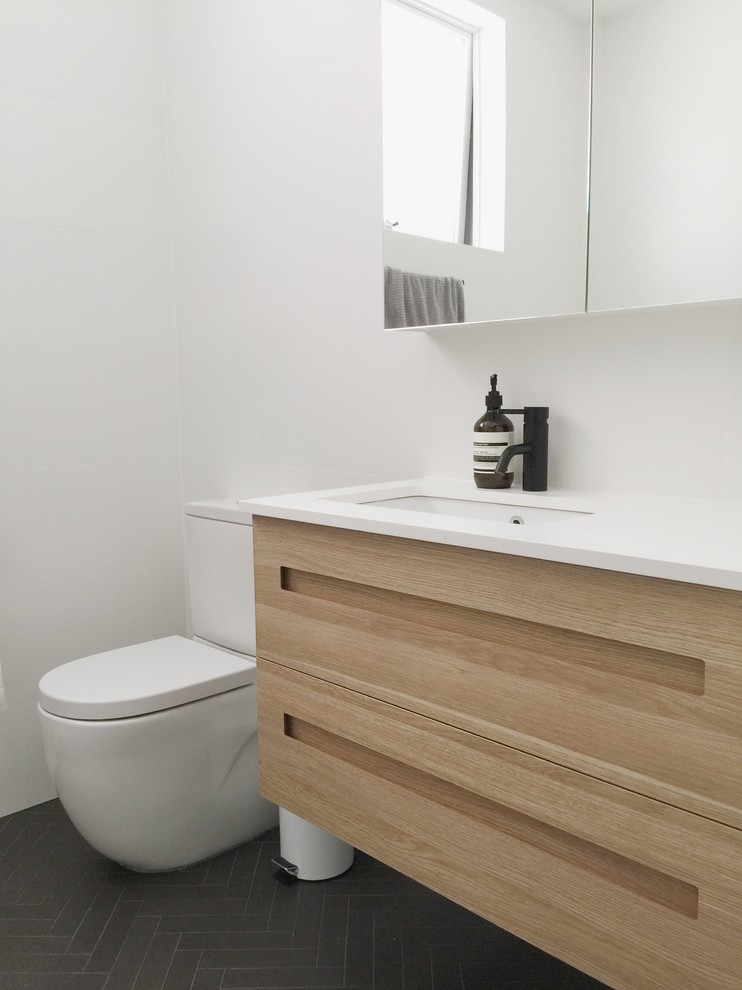 Foto på ett litet nordiskt badrum, med skåp i ljust trä, ett platsbyggt badkar, en dusch/badkar-kombination, en toalettstol med hel cisternkåpa, vit kakel, keramikplattor, vita väggar och ett integrerad handfat