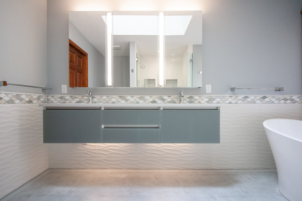 Diseño de cuarto de baño principal minimalista de tamaño medio con puertas de armario azules, bañera exenta, ducha empotrada, baldosas y/o azulejos blancos, lavabo bajoencimera, suelo gris y ducha con puerta con bisagras