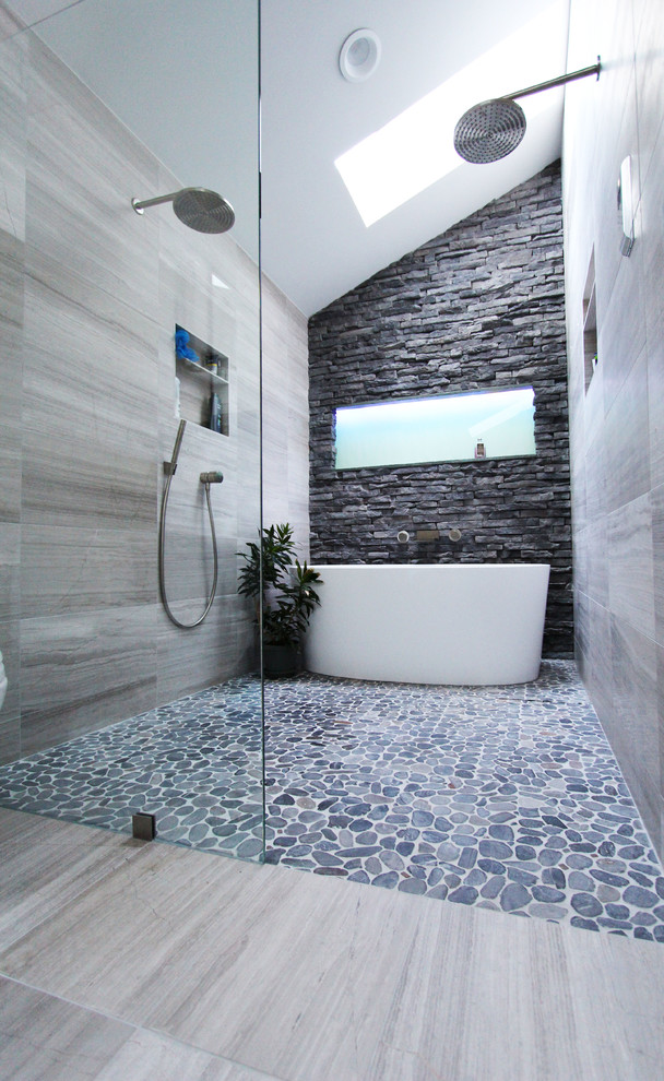 Inspiration for a medium sized contemporary ensuite bathroom in Atlanta with a freestanding bath, a built-in shower, grey tiles, stone tiles, limestone flooring, flat-panel cabinets, grey cabinets, a two-piece toilet, white walls, a vessel sink, granite worktops, grey floors, an open shower, black worktops, a wall niche, double sinks, a floating vanity unit and a vaulted ceiling.