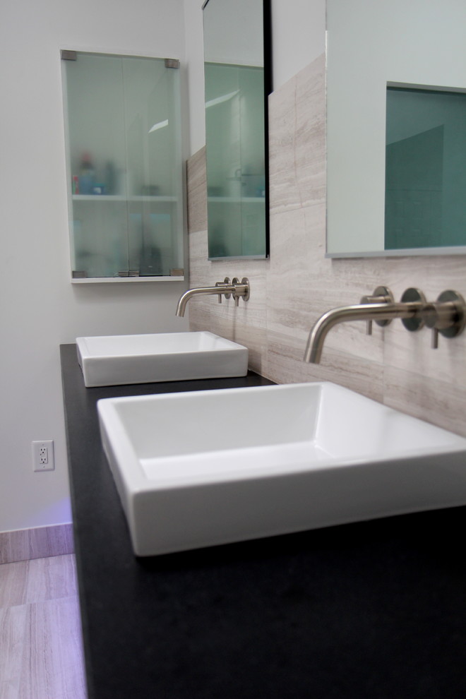 Inspiration for a medium sized contemporary ensuite bathroom in Atlanta with a vessel sink, granite worktops, grey tiles, flat-panel cabinets, grey cabinets, a freestanding bath, a built-in shower, a two-piece toilet, stone tiles, white walls, limestone flooring, grey floors, an open shower, black worktops, a wall niche, double sinks, a floating vanity unit and a vaulted ceiling.
