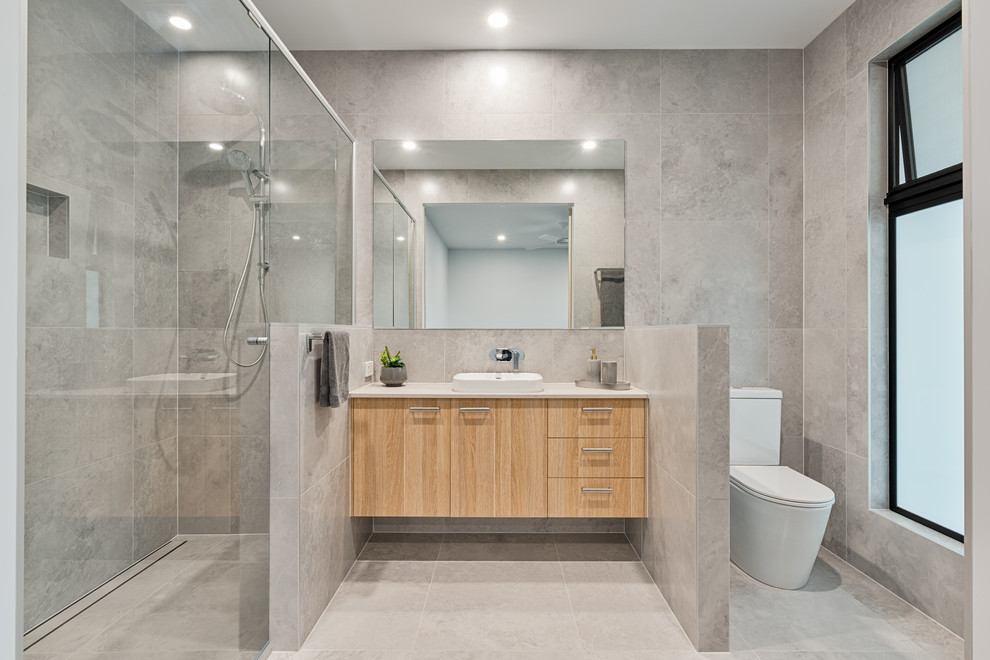 Photo of a contemporary bathroom in Sunshine Coast with flat-panel cabinets, light wood cabinets, an alcove shower, a two-piece toilet, grey tiles, a built-in sink, grey floors and white worktops.