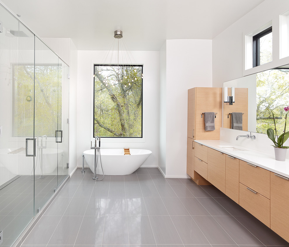 Inspiration for a large contemporary ensuite bathroom in Charleston with flat-panel cabinets, medium wood cabinets, a freestanding bath, a submerged sink, white walls, porcelain flooring, solid surface worktops, grey floors, a hinged door and white worktops.