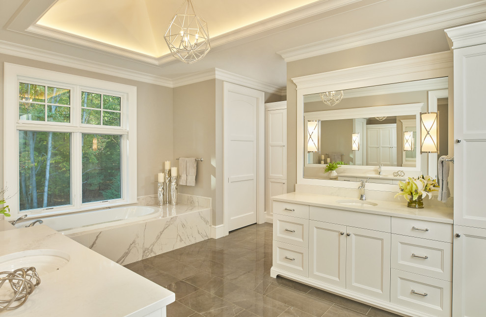 Klassisk inredning av ett stort vit vitt en-suite badrum, med vita skåp, en jacuzzi, marmorgolv, ett undermonterad handfat, bänkskiva i kvarts, grått golv och luckor med infälld panel