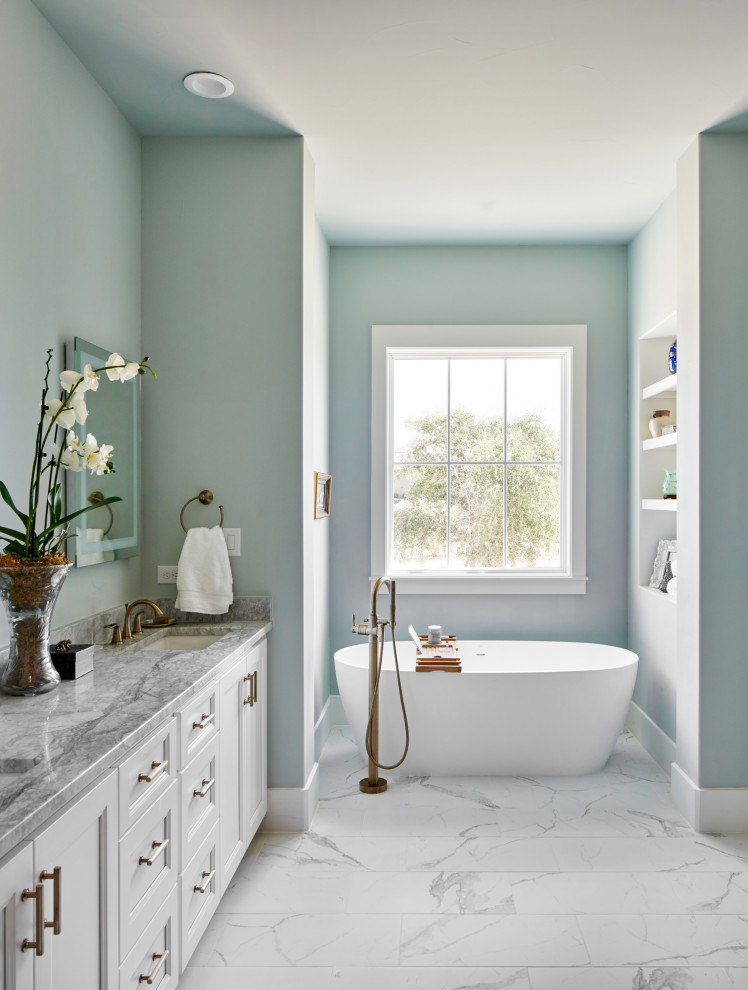 На фото: ванная комната в стиле кантри с фасадами с утопленной филенкой, белыми фасадами, отдельно стоящей ванной, синими стенами, врезной раковиной, белым полом, серой столешницей и зеркалом с подсветкой
