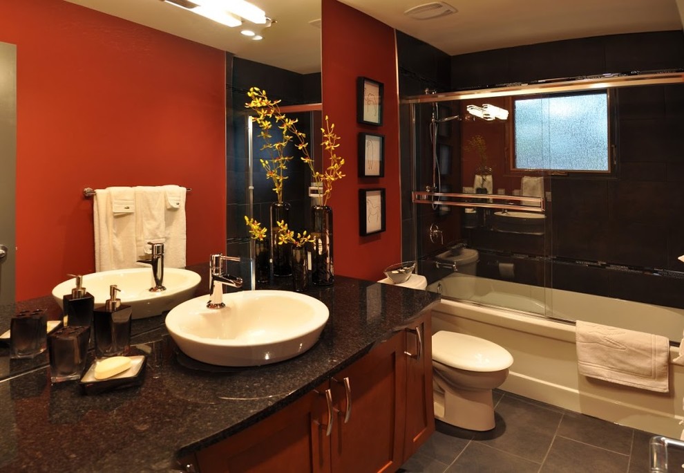 カルガリーにあるお手頃価格の中くらいなアジアンスタイルのおしゃれなバスルーム (浴槽なし) (ベッセル式洗面器、落し込みパネル扉のキャビネット、中間色木目調キャビネット、御影石の洗面台、黒いタイル、セラミックタイル、赤い壁、セラミックタイルの床、アルコーブ型浴槽、シャワー付き浴槽	、引戸のシャワー) の写真