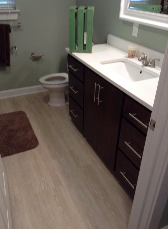 Modelo de cuarto de baño moderno de tamaño medio con armarios con paneles lisos, puertas de armario de madera en tonos medios, baldosas y/o azulejos grises, suelo vinílico, aseo y ducha, lavabo bajoencimera, encimera de cuarzo compacto y suelo blanco