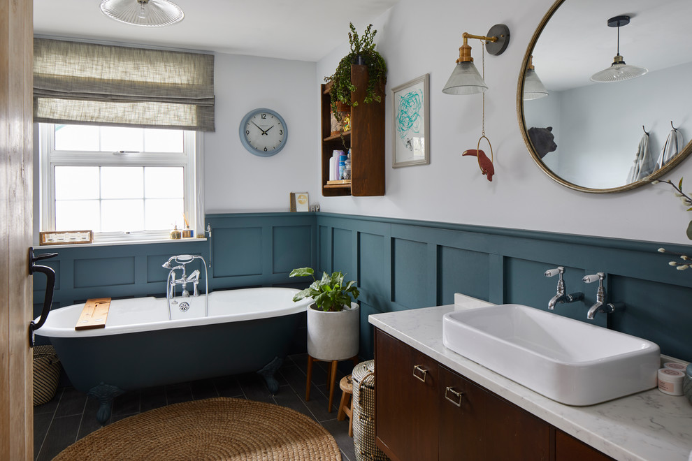 На фото: ванная комната в современном стиле с плоскими фасадами, темными деревянными фасадами, ванной на ножках, белыми стенами, настольной раковиной, серым полом и белой столешницей