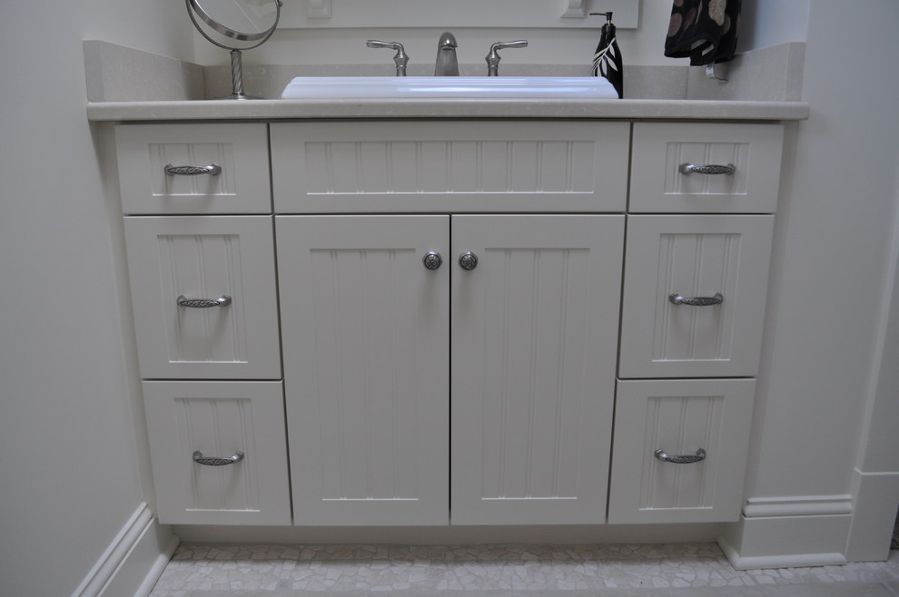 Small coastal shower room bathroom in Other with shaker cabinets, white cabinets, a two-piece toilet, beige tiles, white walls, pebble tile flooring, a built-in sink and solid surface worktops.