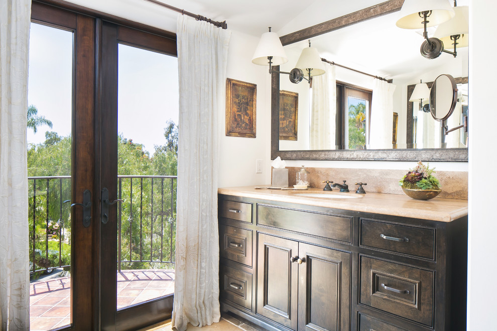 На фото: главная ванная комната среднего размера в средиземноморском стиле с фасадами с утопленной филенкой, темными деревянными фасадами, столешницей из известняка и коричневым полом с