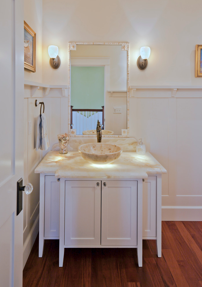 Cette image montre une salle d'eau craftsman de taille moyenne avec un placard à porte shaker, des portes de placard blanches, un plan de toilette en onyx, un carrelage blanc, des carreaux de céramique, un mur blanc, un sol en bois brun, une vasque et un sol marron.