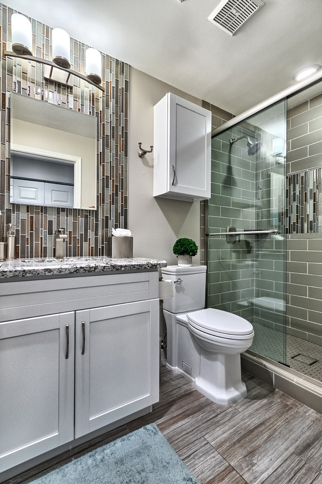 Inredning av ett klassiskt litet grå grått badrum med dusch, med vita skåp, en toalettstol med separat cisternkåpa, grå kakel, grå väggar, klinkergolv i porslin, granitbänkskiva, grått golv, dusch med skjutdörr, skåp i shakerstil, en dusch i en alkov, stickkakel och ett undermonterad handfat