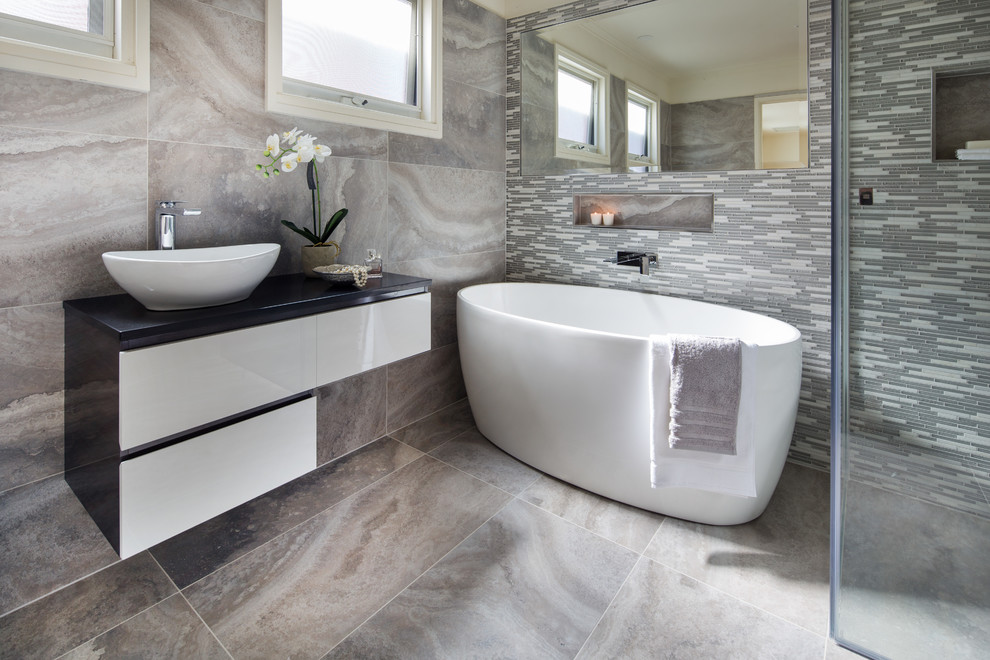 Bild på ett mellanstort funkis badrum med dusch, med släta luckor, vita skåp, ett fristående badkar, grå kakel, vit kakel, ett fristående handfat, porslinskakel och granitbänkskiva