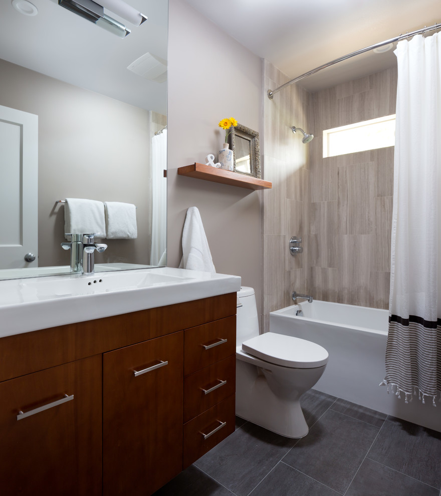 Bild på ett litet funkis badrum med dusch, med släta luckor, skåp i mellenmörkt trä, ett badkar i en alkov, en dusch/badkar-kombination, beige kakel, stenkakel, beige väggar, skiffergolv, ett väggmonterat handfat, en toalettstol med hel cisternkåpa, bänkskiva i akrylsten, grått golv och dusch med duschdraperi