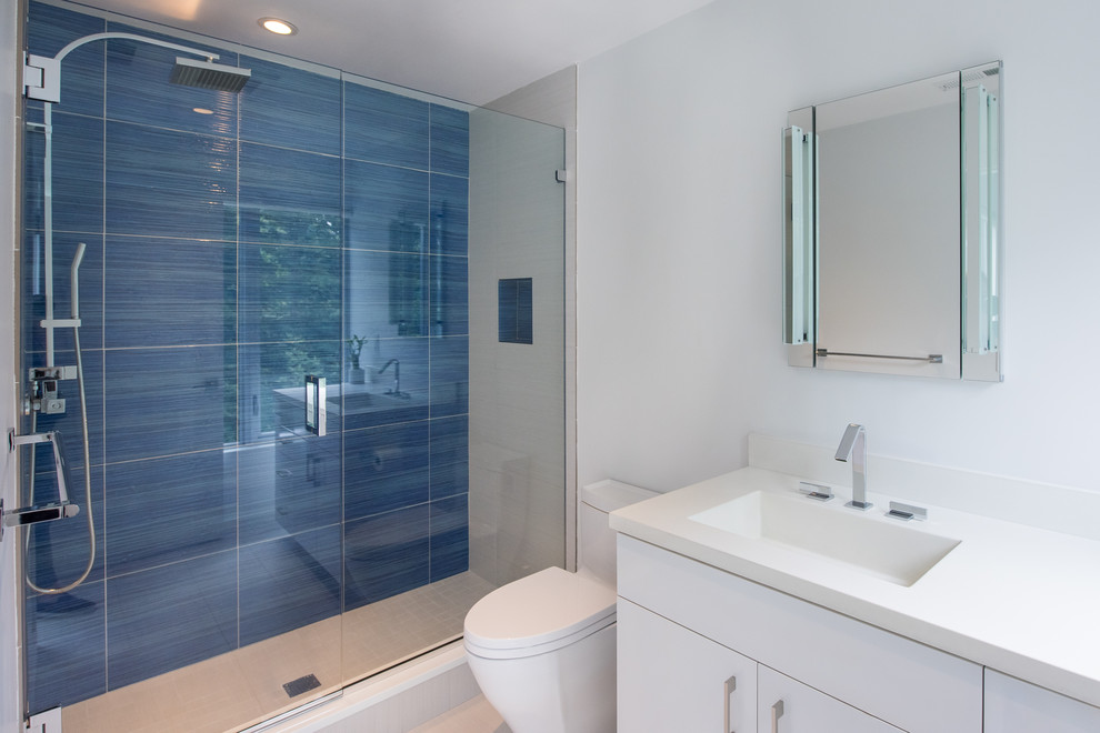 Photo of a large modern family bathroom in New York with flat-panel cabinets, white cabinets, a one-piece toilet, blue tiles, glass tiles, white walls, porcelain flooring, an integrated sink, concrete worktops, white floors and a sliding door.