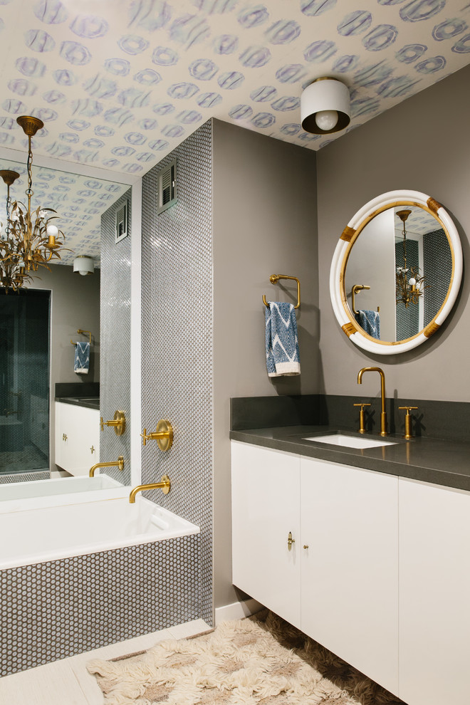 Inspiration pour une salle de bain principale design avec un placard à porte plane, des portes de placard blanches, une baignoire posée, un mur gris, un lavabo encastré et un sol beige.
