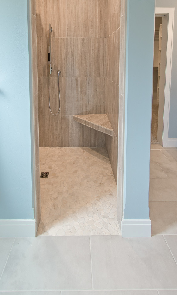 Cette image montre une salle de bain principale traditionnelle avec une douche d'angle, un carrelage beige, des carreaux de porcelaine, un mur bleu, un sol en galet, un sol beige et un banc de douche.