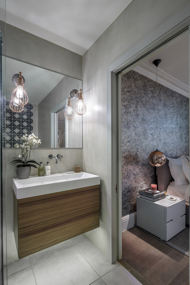 Design ideas for a medium sized bohemian ensuite bathroom in London with flat-panel cabinets, light wood cabinets, a freestanding bath, a walk-in shower, a wall mounted toilet, multi-coloured tiles, cement tiles, grey walls, ceramic flooring, a trough sink, grey floors, a sliding door and white worktops.