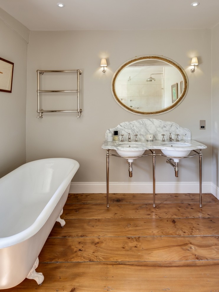 Cette image montre une salle de bain principale craftsman avec une baignoire sur pieds, un carrelage beige, des dalles de pierre, un mur gris, un plan vasque et un plan de toilette en marbre.
