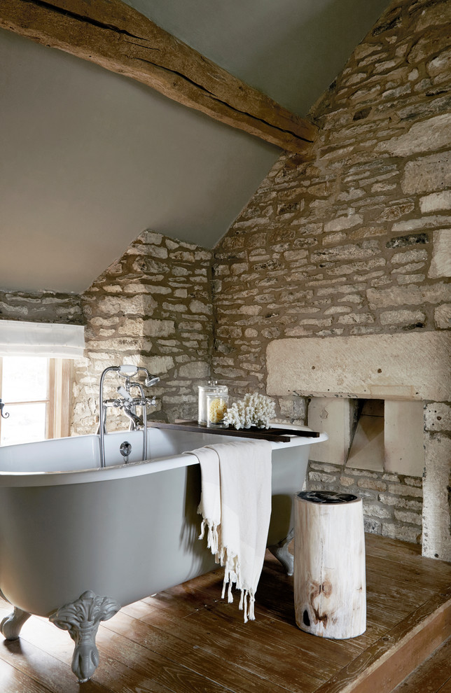 Réalisation d'une salle de bain champêtre avec une baignoire sur pieds, parquet foncé, un sol marron et un mur en pierre.