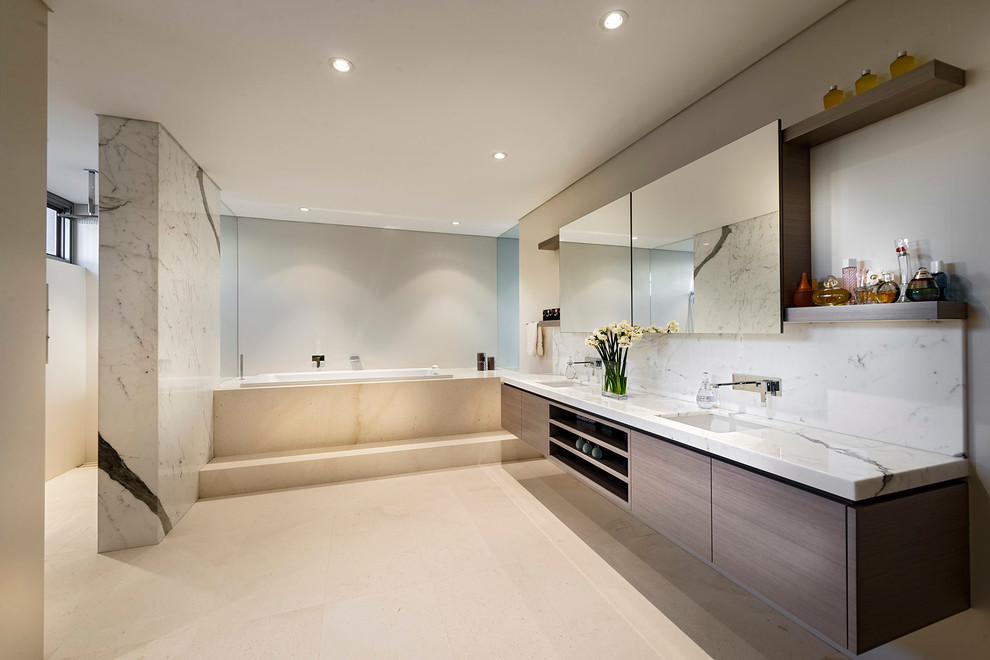 Diseño de cuarto de baño actual con lavabo bajoencimera, armarios con paneles lisos, bañera encastrada, paredes beige, encimeras blancas y piedra