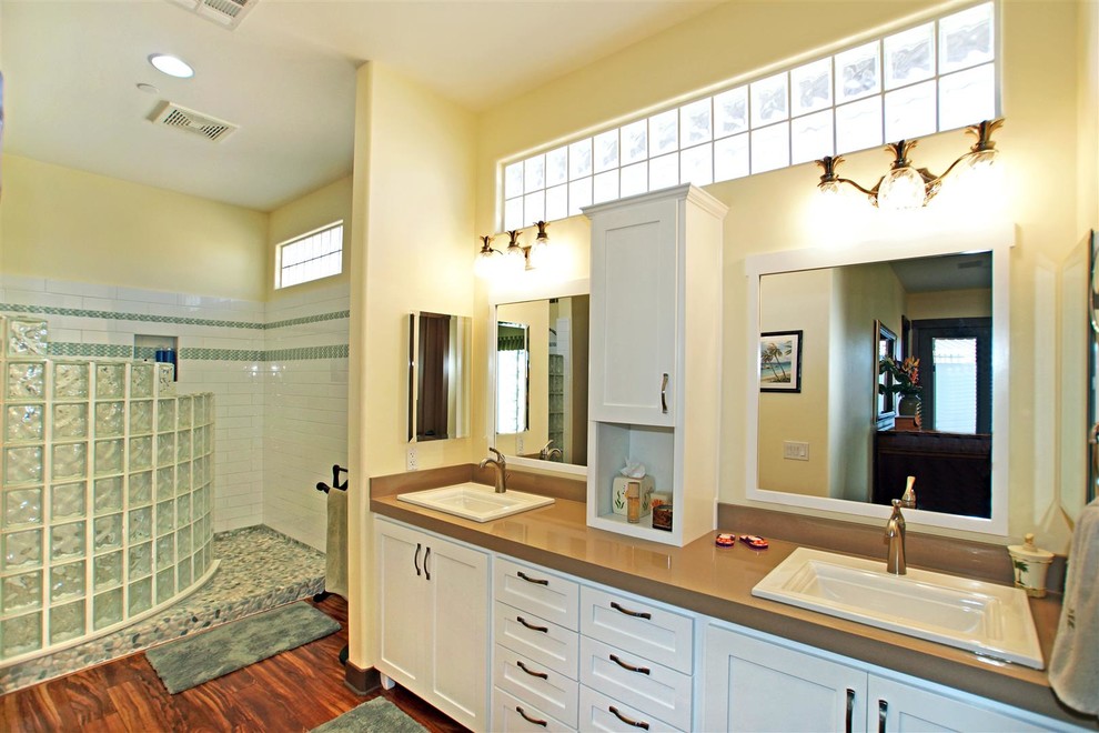 Mittelgroßes Klassisches Badezimmer mit Schrankfronten im Shaker-Stil, weißen Schränken, Duschnische, gelber Wandfarbe, dunklem Holzboden, Einbauwaschbecken und Mineralwerkstoff-Waschtisch in Las Vegas