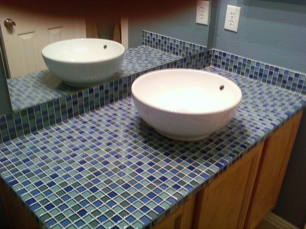 Cette photo montre une salle d'eau chic en bois brun de taille moyenne avec un placard avec porte à panneau encastré, un carrelage bleu, mosaïque, un mur bleu, une vasque, un plan de toilette en carrelage et un plan de toilette bleu.