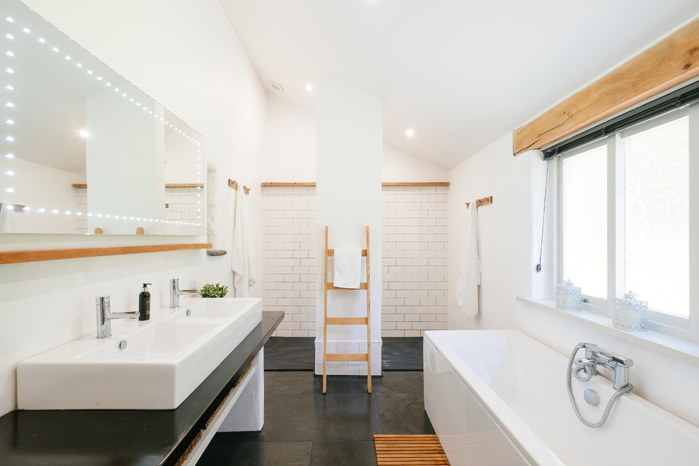 This is an example of a rural ensuite bathroom in Cornwall with a freestanding bath, a built-in shower, white tiles, white walls, a vessel sink, grey floors, an open shower and black worktops.