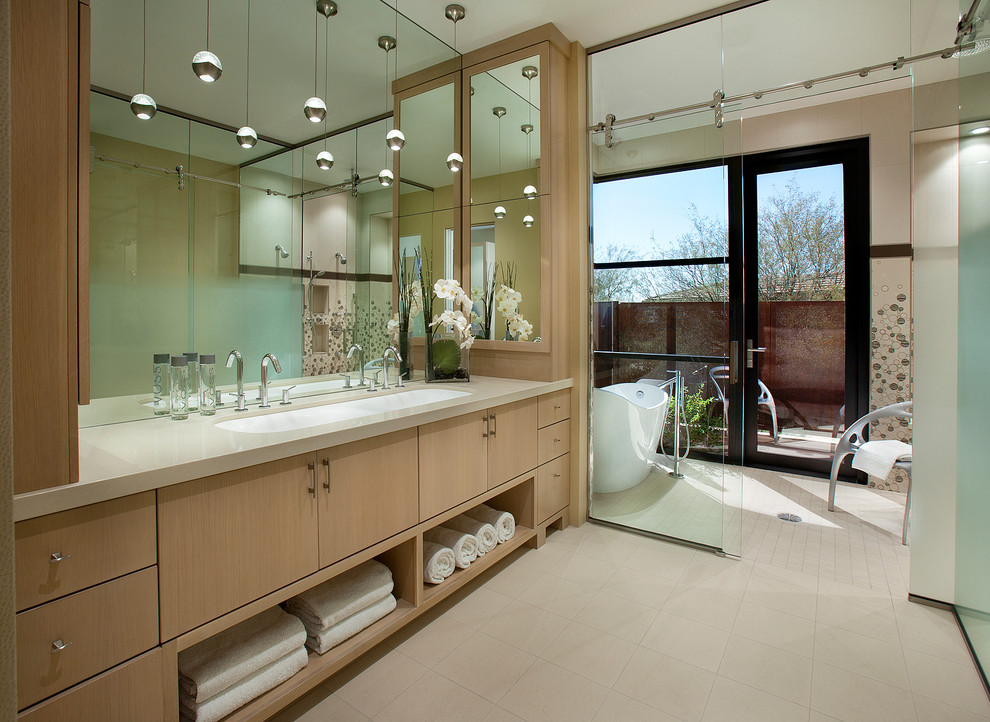 Идея дизайна: ванная комната в современном стиле с раковиной с несколькими смесителями, плоскими фасадами, светлыми деревянными фасадами и отдельно стоящей ванной