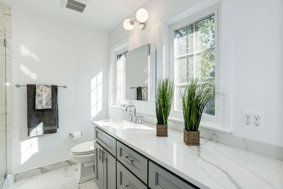 Inspiration for a mid-sized transitional master white tile and ceramic tile porcelain tile and white floor alcove shower remodel in DC Metro with shaker cabinets, gray cabinets, a one-piece toilet, white walls, an undermount sink, quartz countertops, a hinged shower door and white countertops