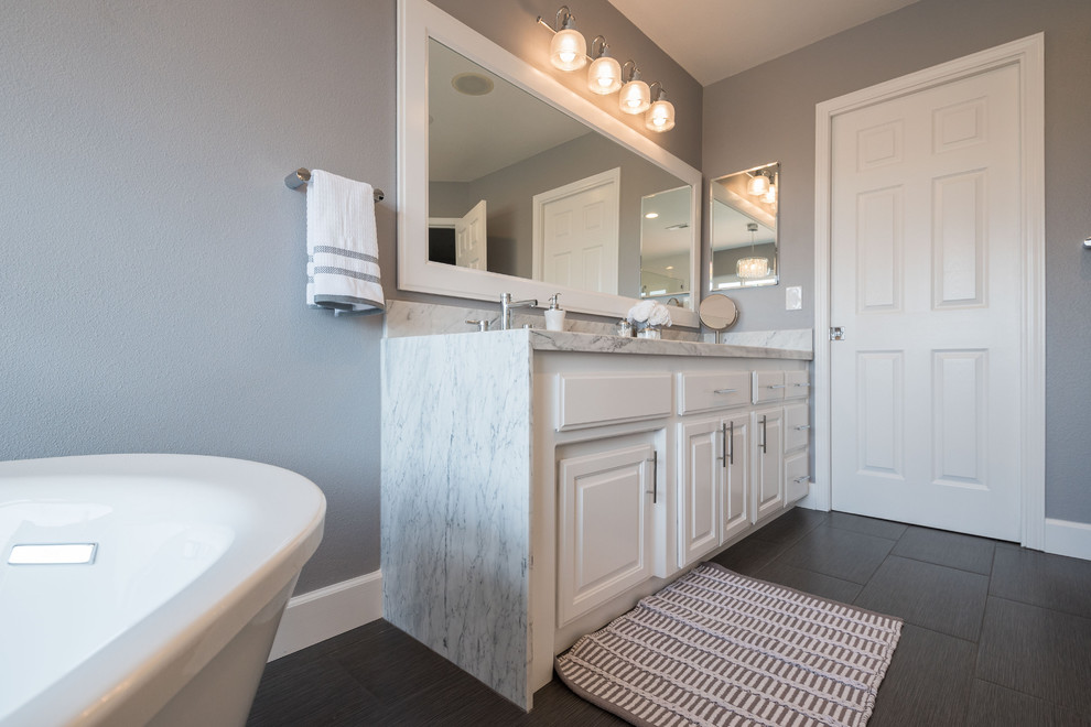 Cette photo montre une grande salle de bain principale tendance avec un placard avec porte à panneau surélevé, des portes de placard blanches, un mur gris, un sol en carrelage de porcelaine, un lavabo encastré, un plan de toilette en quartz et un sol marron.