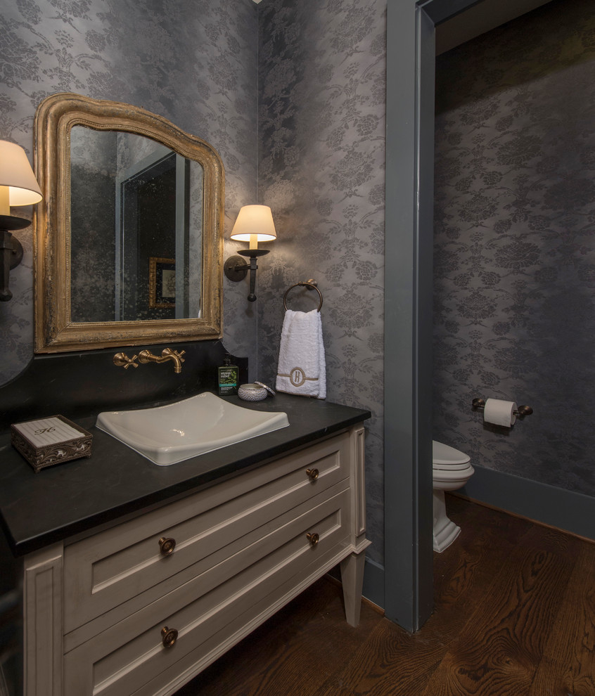 Klassisk inredning av ett litet svart svart badrum, med möbel-liknande, beige skåp, en toalettstol med hel cisternkåpa, svarta väggar, mörkt trägolv, ett nedsänkt handfat, bänkskiva i täljsten och brunt golv